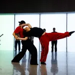 Two dancers create a balance, with one bending back and extending her left leg (right) while the other supports (left).