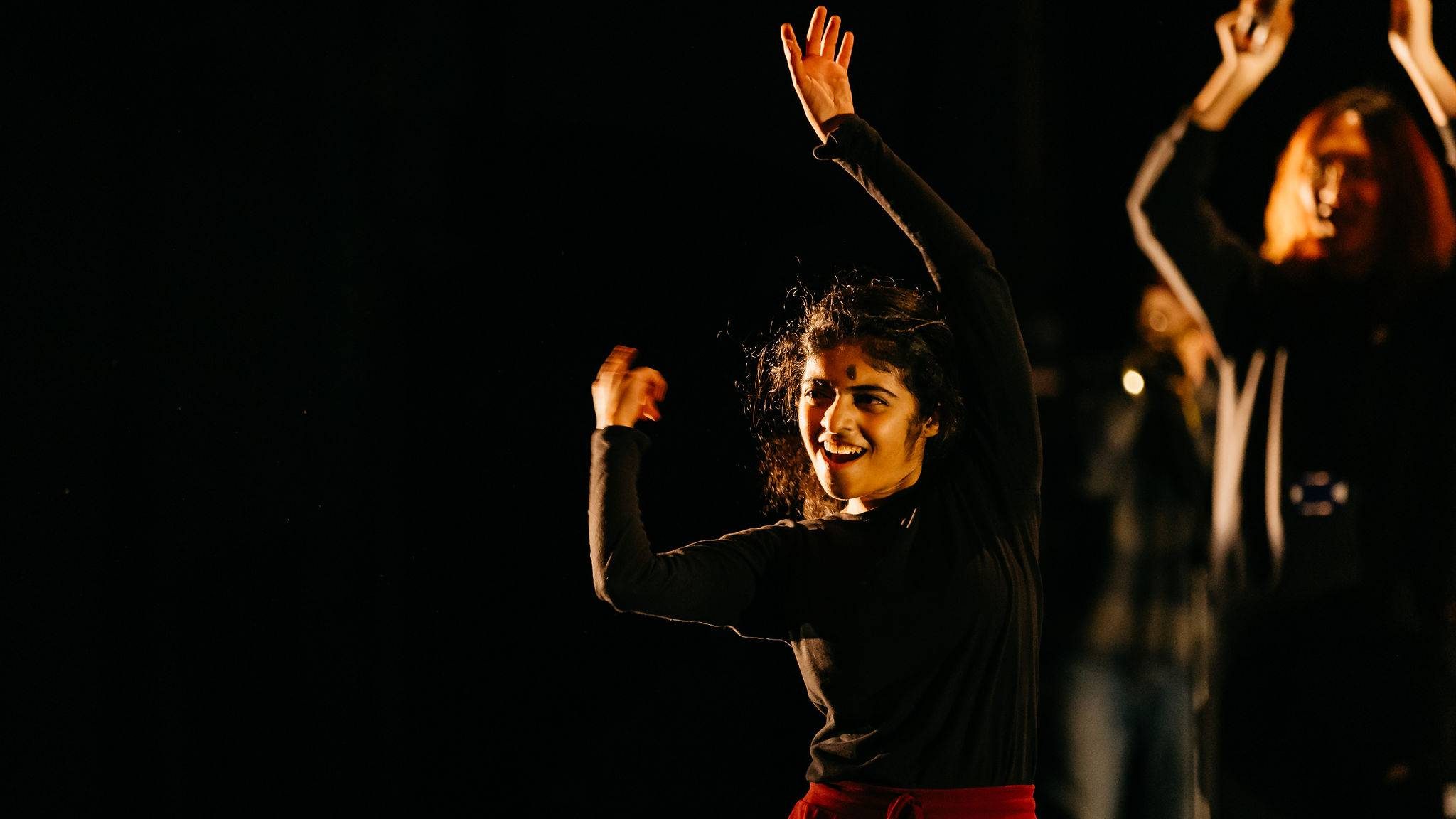 A student wearing a black top and red trousers dances on stage