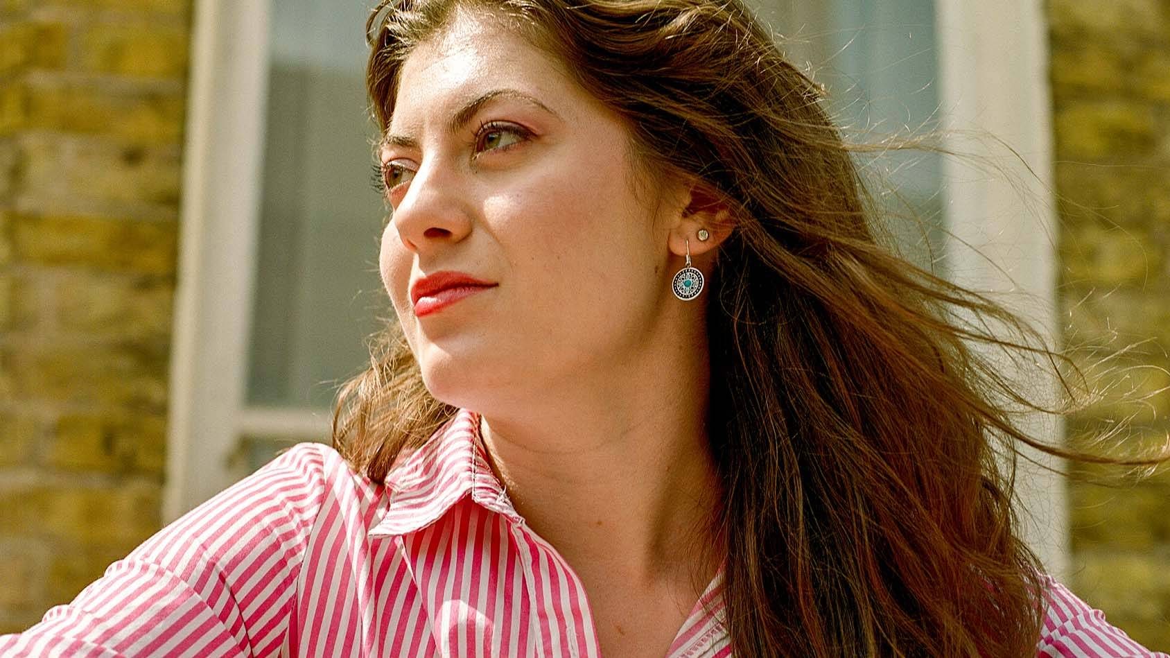 A musical theatre student with long hair and a striped dress stands in front of a window