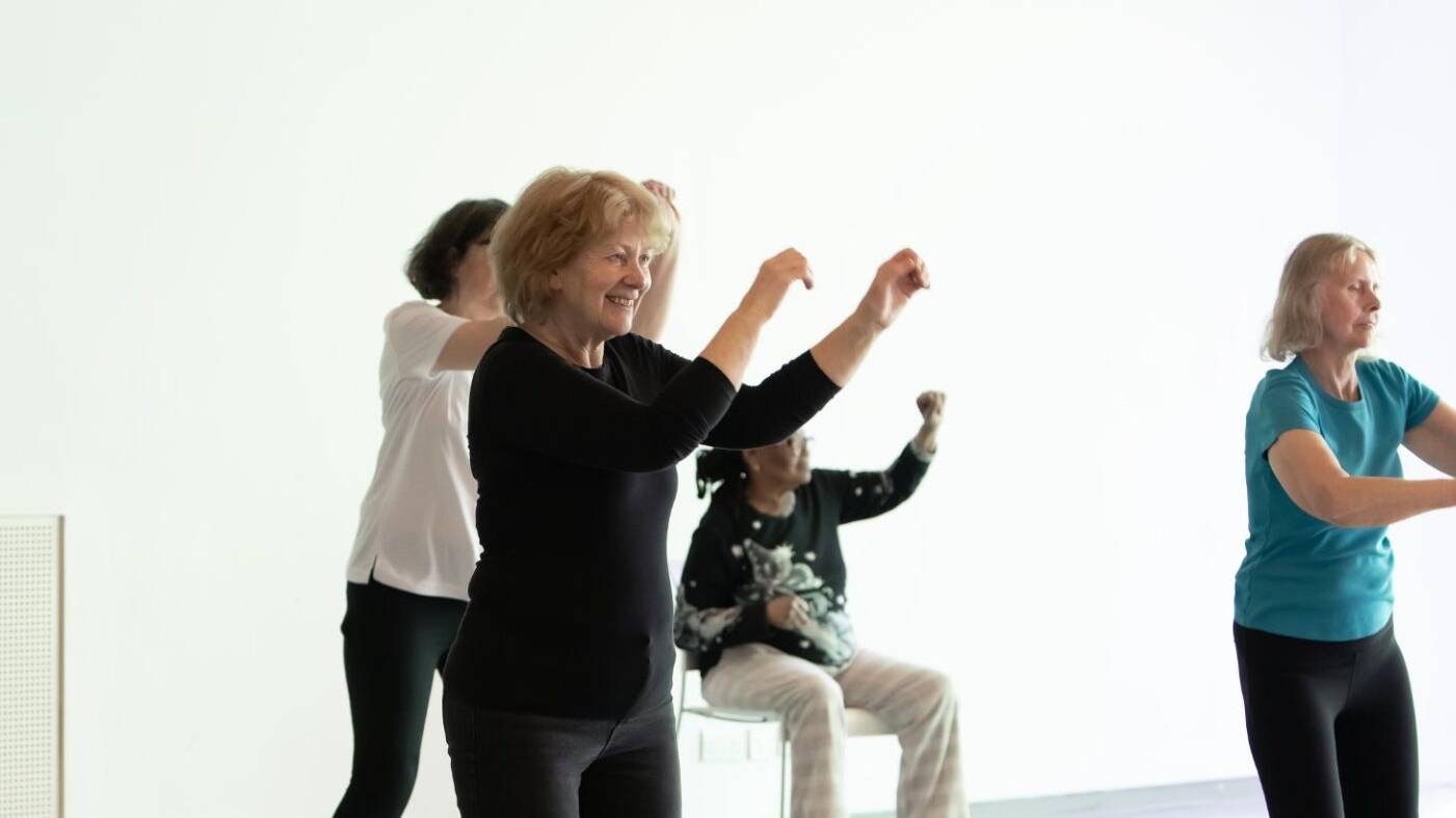 Group of over adults with various levels of mobility move in unison during Creative Dance class for over 60s at Trinity Laban.