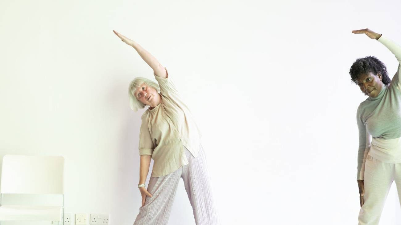 Two participants hold an over arm stretch warming up for a Dynamic Dance Class for over 60s at Trinity Laban