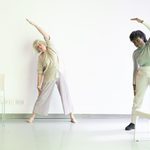 Two participants hold an over arm stretch warming up for a Dynamic Dance Class for over 60s at Trinity Laban