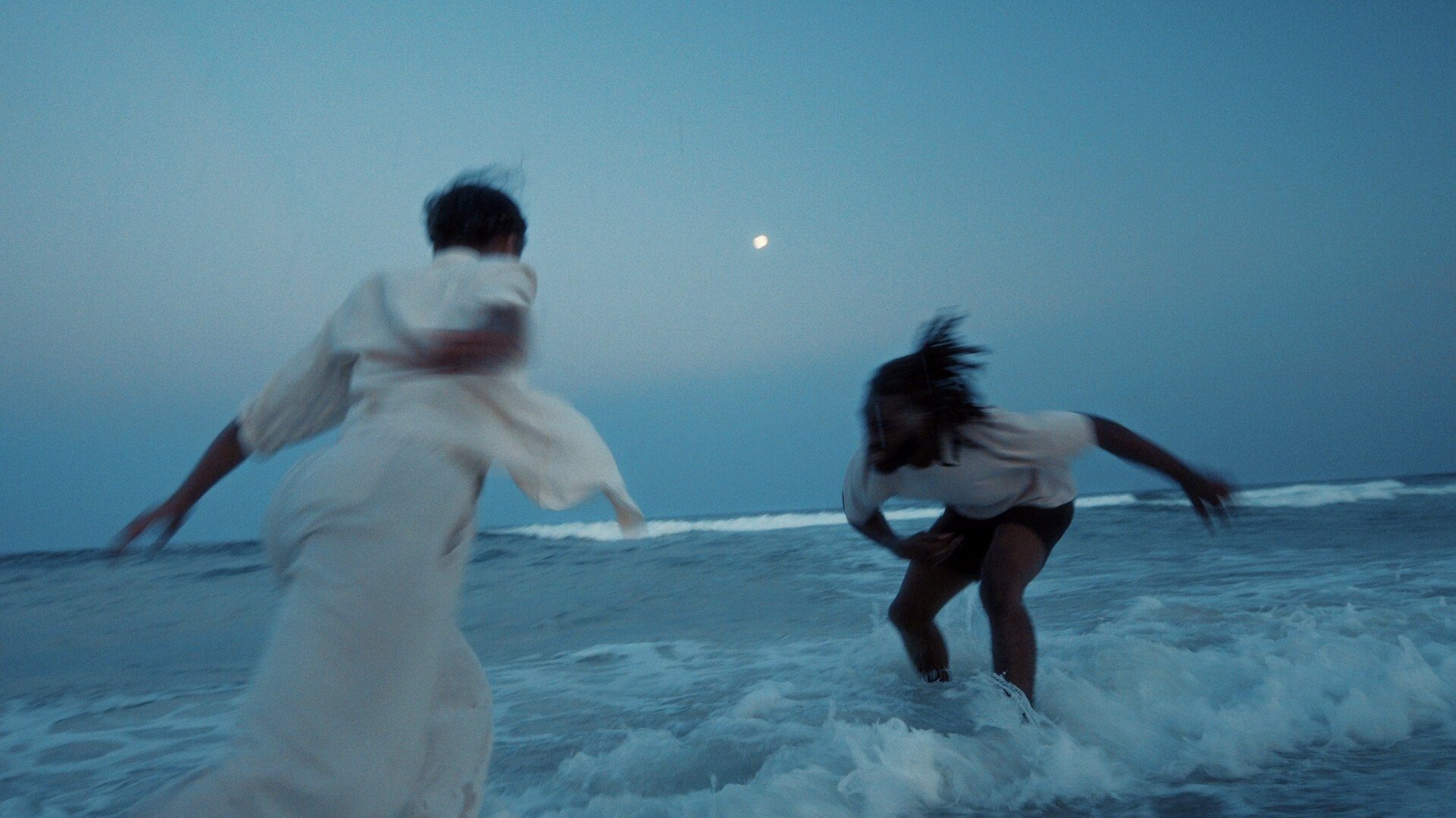 Two people dancing in the sea with the moon in the background.