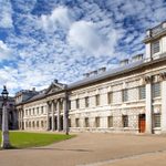 Trinity Laban's King Charles Court building in Greenwich. The building is white stone, and there is a green lawn in front of it.