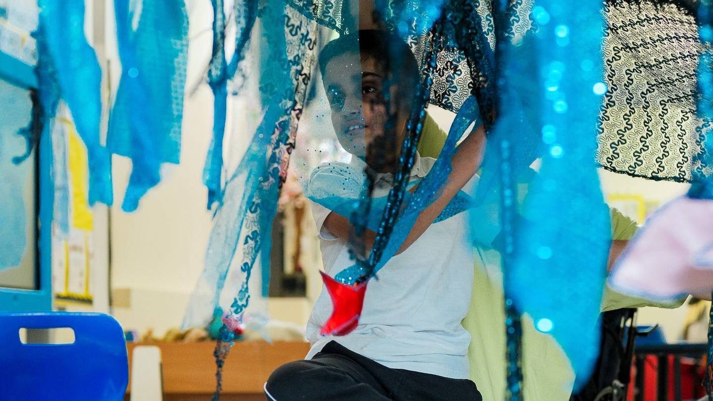 A young person plays with multicoloured fabric which hangs from above him.