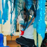 A young person plays with multicoloured fabric which hangs from above him.