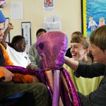 Two artists show a young person a purple, metallic material octopus.