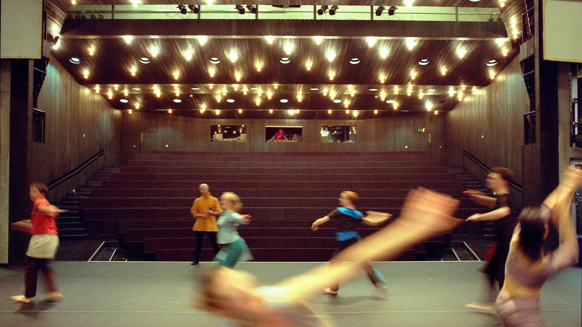 A group of dancers on stage, in the background you can see the raked seating and sound/light desk.