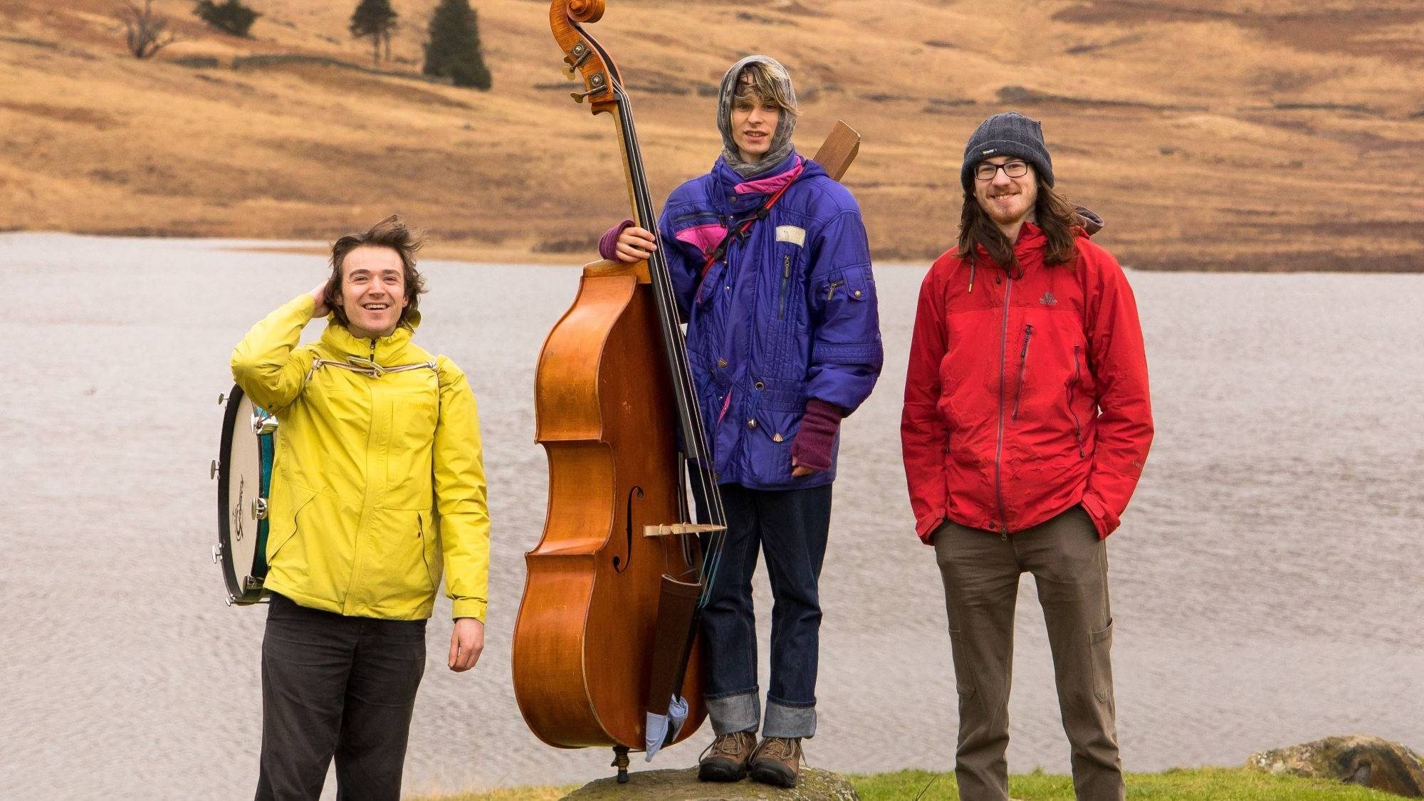 Jazz trio EMRYS stand in front of a lake.
