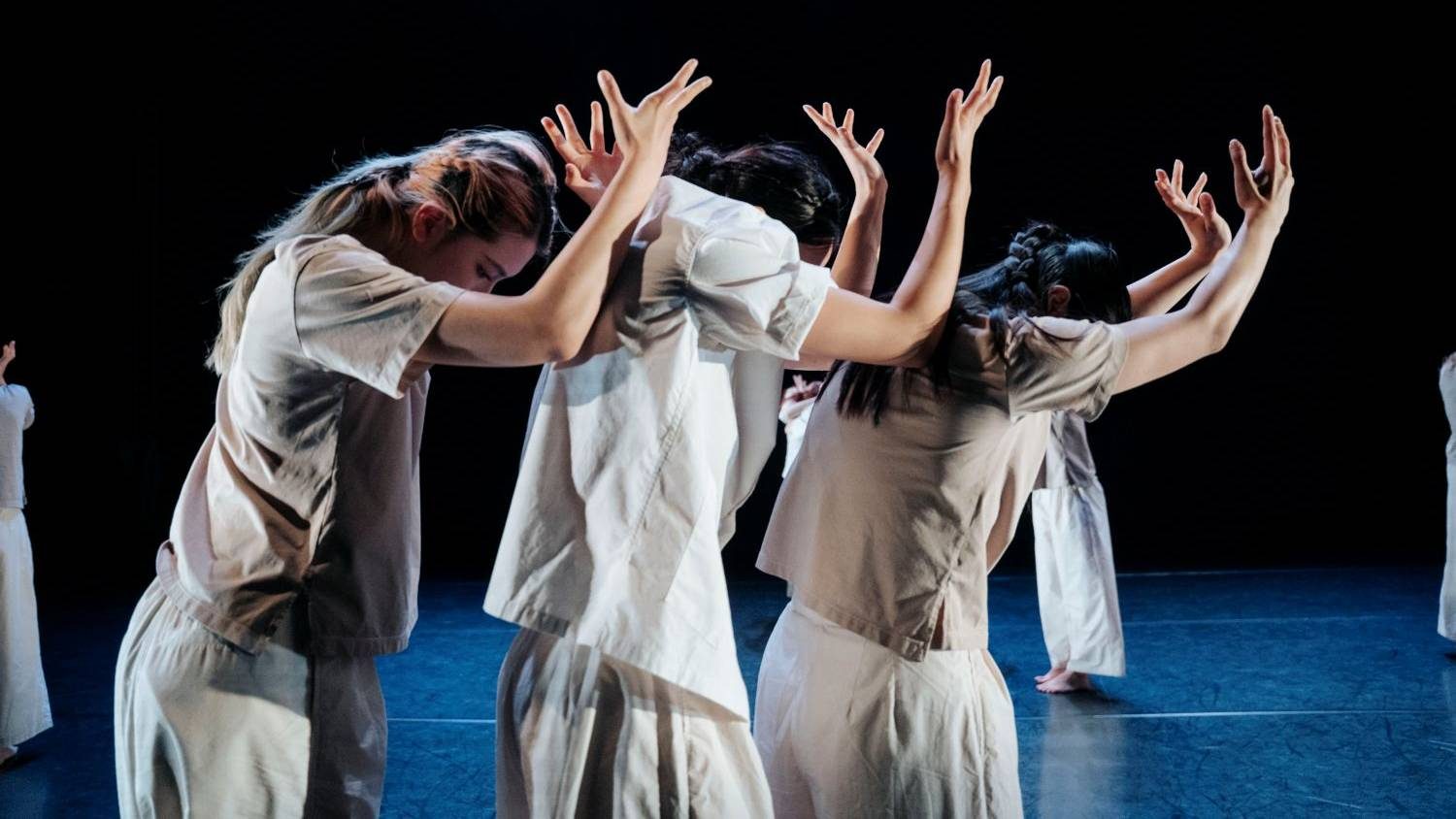 Three dancers from Trinity Laban Dance Collective are at the front of the stage, with their heads bowed and arms in the air.