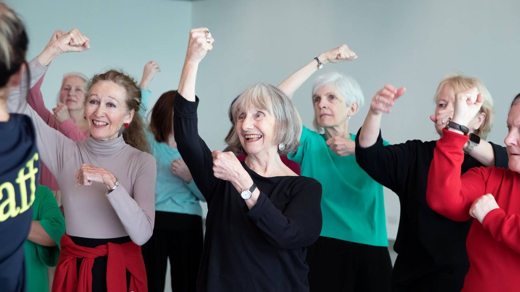 summer series over 60s, class with their arms raised and smiling at the tutor